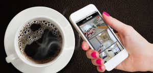 Taza de café y mano que sostiene un smartphone con control desde App de las imágenes que ofrecen las cámaras de seguridad de AUNSOLO Click de la videovigilancia del interior de una casa